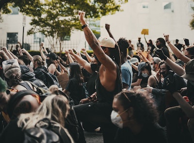 A group of people, most with one arm raised with the hand in a fist. Many of the people wear face masks.