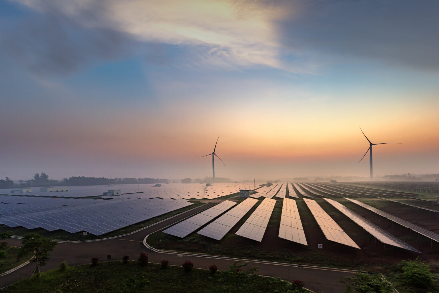 Solar panels and wind turbines in the background, while the sun rises in the sky.