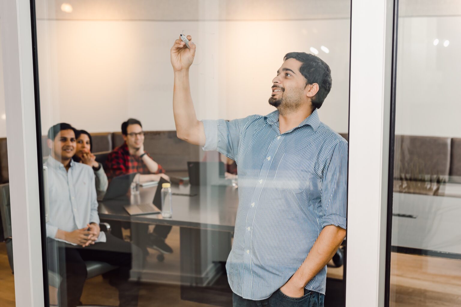 Employees brainstorming at a glass whiteboard in a boardroom.