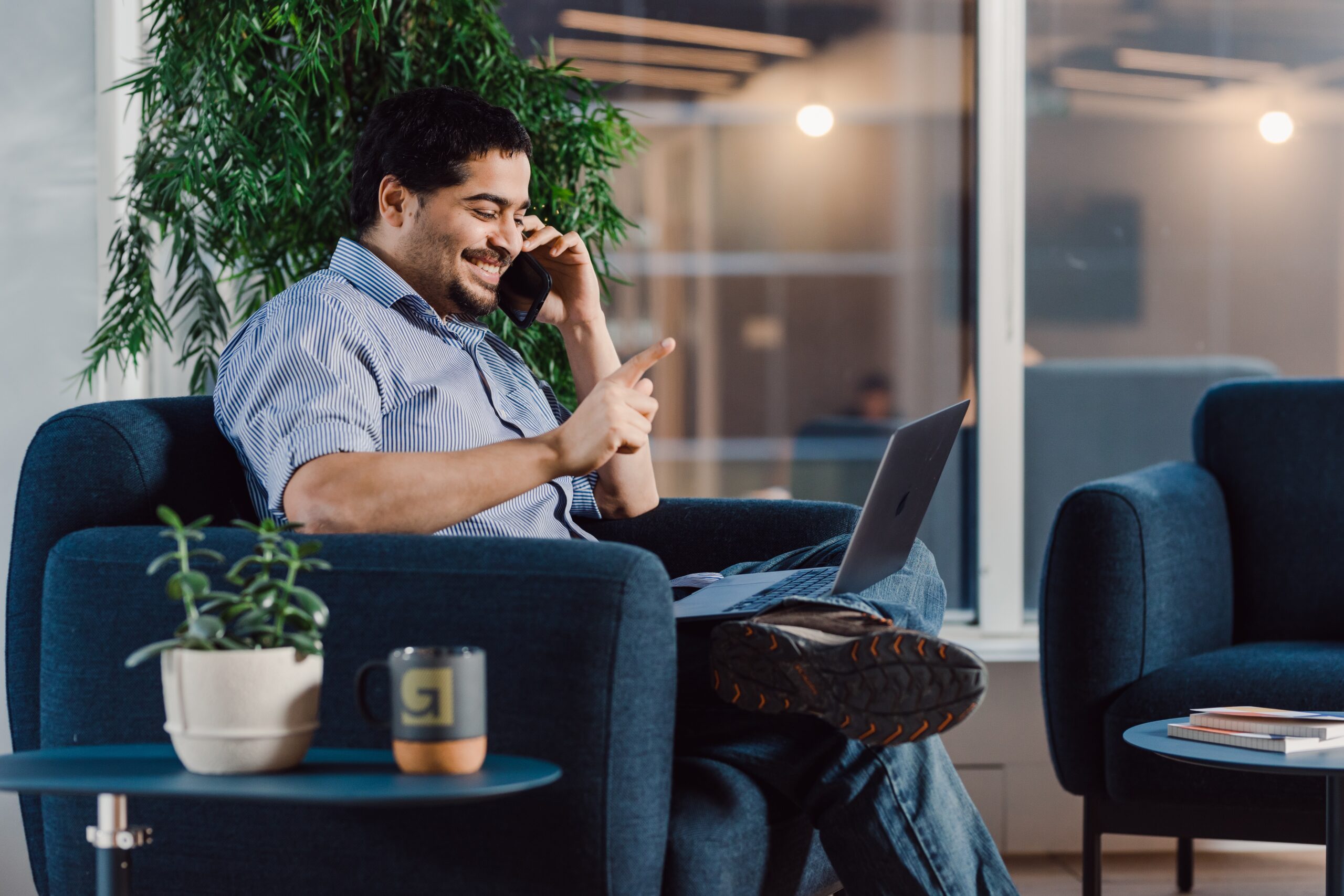 A person is smiling and having a conversation on the phone while looking at a laptop